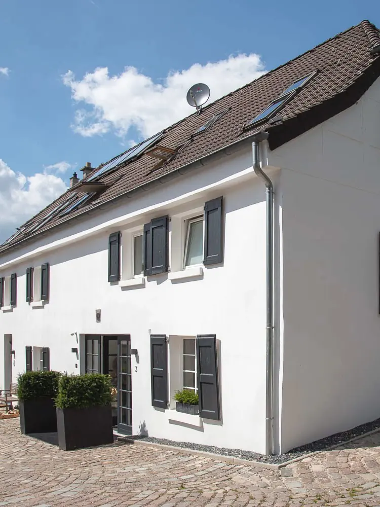 Die Praxis Schönheitsmühle in Ratingen: ein weiß gekalktes Mühlengebäude mit dunklen Fensterläden am Kopfsteinhof